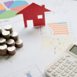 With House Model And Stack Of Coins On Desk