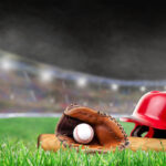 Baseball helmet, bat, glove and ball on grass in brightly lit outdoor stadium. Focus on foreground and shallow depth of field on background with copy space. Fictitious background stadium created entirely in Photoshop.