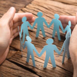 Cropped image of businessman's hands covering paper team on wooden table