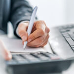 Photo of Male accountant calculations and analyzing data with calculator, Financing, Accounting, Doing finance, Economy, Savings Banking Concept. Close up, business man or lawyer accountant working on accounts using a calculator and writing on documents while sitting on his desk in modern office.