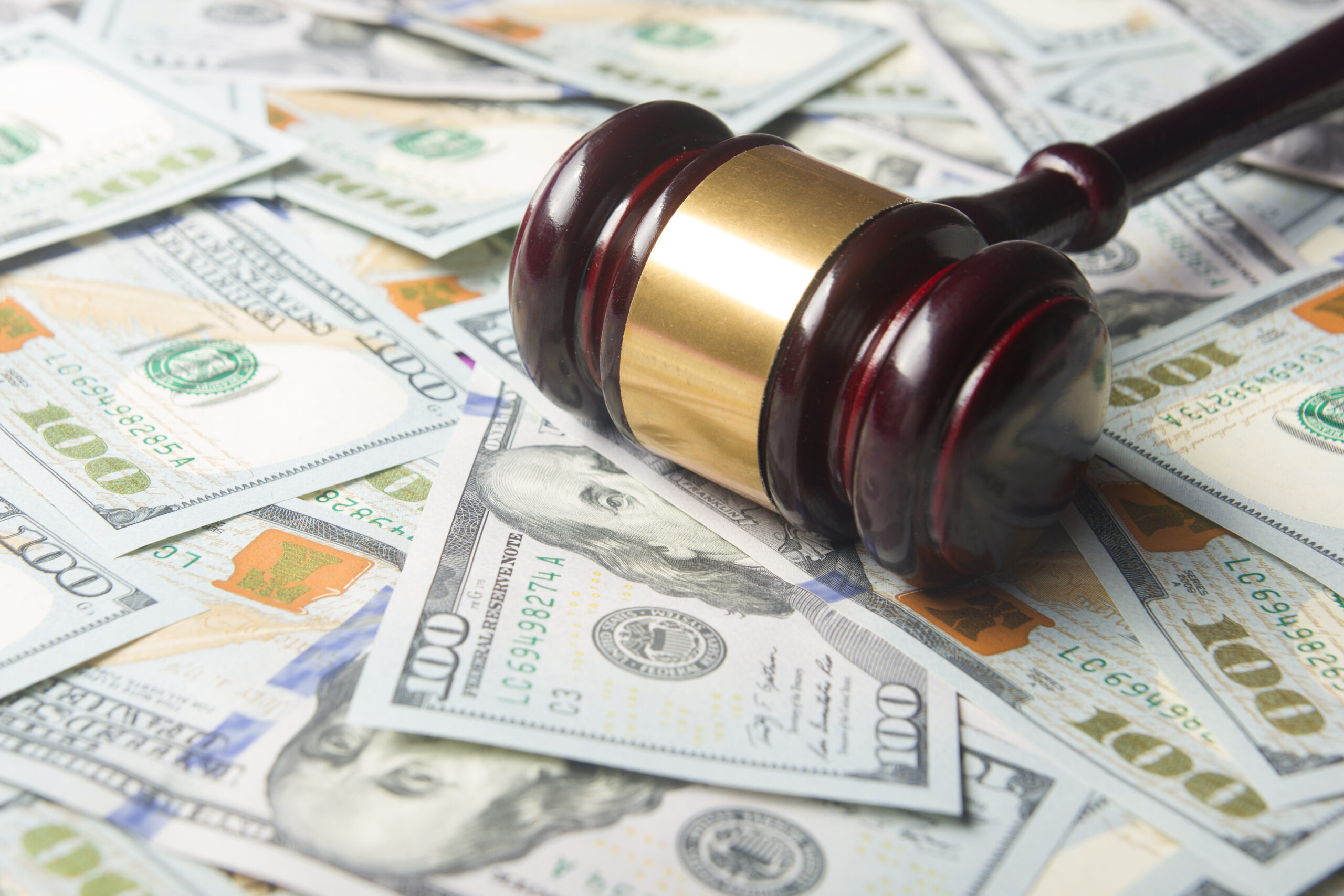 A brown wooden gavel sits on top of a pile of new one-hundred-dollar bills.