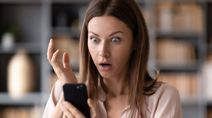 A startled woman raises her hand while seeing concerning images on her cell phone.
