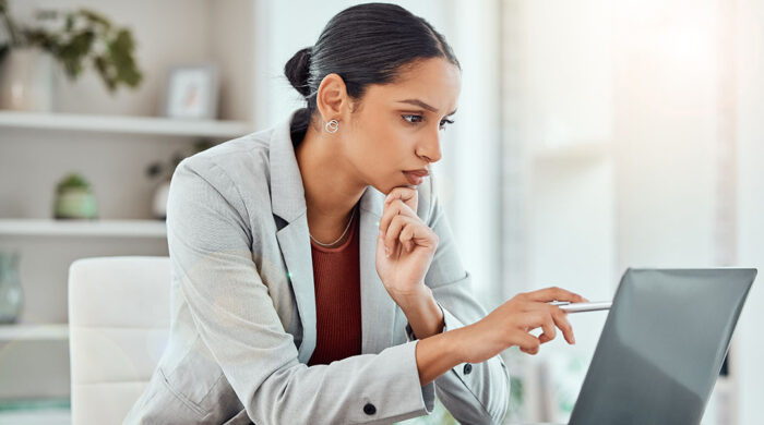 A female defamation attorney sits at a desk and reviews a defamation lawsuit on her laptop.