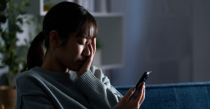 Young depressed woman with her head in her hands looking at her phone.